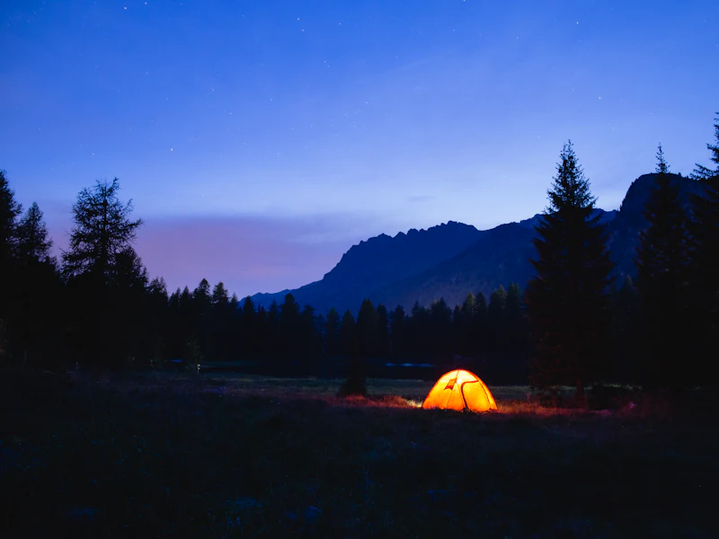 Beleuchtetes Zelt zur blauen Stunde vor einer Bergkette