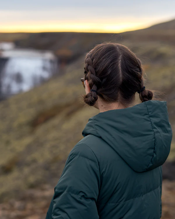 Frau in grüner Outdoorjacke blickt über eine weite Landschaft